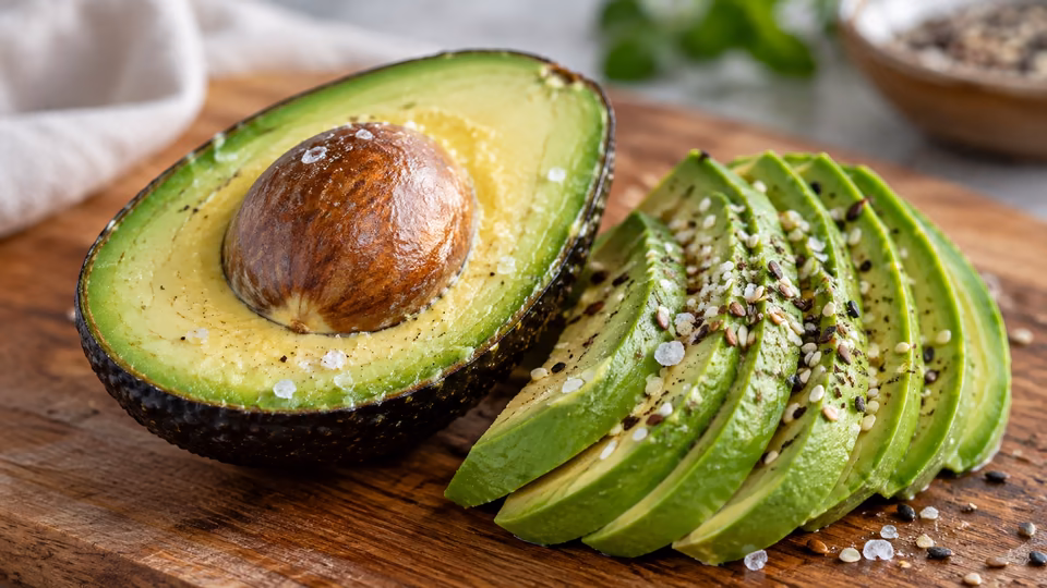 An avocado half and slices on a wooden board.